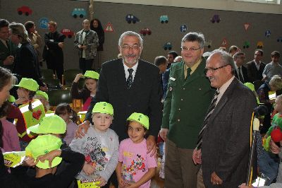 Der Regierungspr�sident, der Polizeivizepr�sident und ein weiterer Ehrengast verteilen Baseballk�ppis und Sicherheitswesten an die Schulkinder